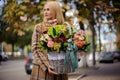 Young and beautiful blonde woman holding a big wicker basket of flowers against the city Royalty Free Stock Photo