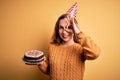 Young beautiful blonde woman holding birthday cake over isolated yellow background with happy face smiling doing ok sign with hand Royalty Free Stock Photo