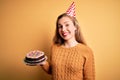 Young beautiful blonde woman holding birthday cake over isolated yellow background with a happy face standing and smiling with a Royalty Free Stock Photo