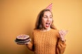 Young beautiful blonde woman holding birthday cake over isolated yellow background pointing and showing with thumb up to the side Royalty Free Stock Photo