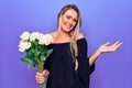 Young beautiful blonde woman holding bouquet of flowers over isolated purple background celebrating achievement with happy smile Royalty Free Stock Photo