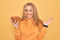 Young beautiful blonde woman holding bowl with healthy almonds over yellow background celebrating victory with happy smile and Royalty Free Stock Photo