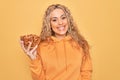 Young beautiful blonde woman holding bowl with healthy almonds over yellow background looking positive and happy standing and Royalty Free Stock Photo