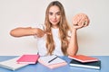 Young beautiful blonde woman holding brain while studying for school pointing finger to one self smiling happy and proud