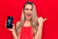 Young beautiful blonde woman holding broken smartphone showing cracked screen pointing thumb up to the side smiling happy with Royalty Free Stock Photo