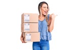 Young beautiful blonde woman holding delivery boxes pointing thumb up to the side smiling happy with open mouth Royalty Free Stock Photo