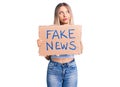 Young beautiful blonde woman holding fake news banner serious face thinking about question with hand on chin, thoughtful about