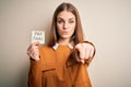 Young beautiful blonde woman holding pay taxes to goverment reminder over yellow background pointing with finger to the camera and