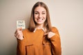 Young beautiful blonde woman holding pay taxes to goverment reminder over yellow background with surprise face pointing finger to