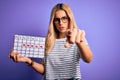 Young beautiful blonde woman holding period calendar to control menstrual cycle pointing with finger to the camera and to you, Royalty Free Stock Photo