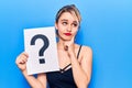 Young beautiful blonde woman holding question mark serious face thinking about question with hand on chin, thoughtful about Royalty Free Stock Photo