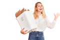 Young beautiful blonde woman holding recycle paper bin celebrating victory with happy smile and winner expression with raised Royalty Free Stock Photo