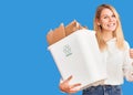 Young beautiful blonde woman holding recycle paper bin smiling happy and positive, thumb up doing excellent and approval sign Royalty Free Stock Photo