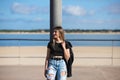 Young, beautiful blonde woman leaning against a lamppost. The woman is dressed in casual clothes and wears a black leather jacket Royalty Free Stock Photo