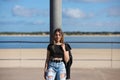 Young, beautiful blonde woman leaning against a lamppost. The woman is dressed in casual clothes and wears a black leather jacket Royalty Free Stock Photo