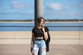 Young, beautiful blonde woman leaning against a lamppost. The woman is dressed in casual clothes and wears a black leather jacket Royalty Free Stock Photo