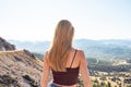 Young beautiful blonde woman looks at the horizon. The traveler stands in the mountains