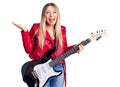 Young beautiful blonde woman playing electric guitar celebrating victory with happy smile and winner expression with raised hands Royalty Free Stock Photo