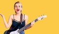 Young beautiful blonde woman playing electric guitar celebrating victory with happy smile and winner expression with raised hands Royalty Free Stock Photo