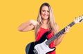 Young beautiful blonde woman playing electric guitar pointing finger to one self smiling happy and proud Royalty Free Stock Photo