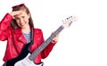 Young beautiful blonde woman playing electric guitar stressed and frustrated with hand on head, surprised and angry face Royalty Free Stock Photo