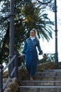 Young beautiful blonde woman with a ponytail in her hair dressed in a denim dress on the steps of the monument in the park in Royalty Free Stock Photo