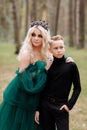 Young beautiful blonde woman queen with young boy in black outfit. Princess mother walks with son. autumn green forest mystic. Royalty Free Stock Photo