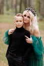 Young beautiful blonde woman queen with young boy in black outfit. Princess mother walks with son. autumn green forest mystic. Royalty Free Stock Photo