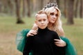 Young beautiful blonde woman queen with young boy in black outfit. Princess mother walks with son. autumn green forest mystic. Royalty Free Stock Photo