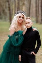 Young beautiful blonde woman queen with young boy in black outfit. Princess mother walks with son. autumn green forest mystic. Royalty Free Stock Photo