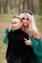 Young beautiful blonde woman queen with young boy in black outfit. Princess mother walks with son. autumn green forest mystic. Royalty Free Stock Photo