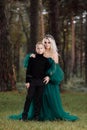 Young beautiful blonde woman queen with young boy in black outfit. Princess mother walks with son. autumn green forest mystic. Royalty Free Stock Photo