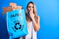 Young beautiful blonde woman recycling holding paper recycle bag full of paperboard covering mouth with hand, shocked and afraid Royalty Free Stock Photo