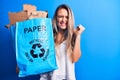 Young beautiful blonde woman recycling holding paper recycle bag full of paperboard screaming proud, celebrating victory and Royalty Free Stock Photo