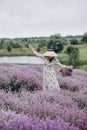 Young beautiful blonde woman in a romantic dress, a straw hat and a basket of flowers dancing in a lavender field. Soft selective Royalty Free Stock Photo