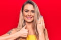 Young beautiful blonde woman showing engagement ring over isolated red background smiling happy and positive, thumb up doing Royalty Free Stock Photo