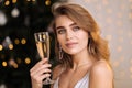 A young beautiful blonde woman in a silver cocktail dress holds a glass of champagne. Smiling and posing against the Royalty Free Stock Photo