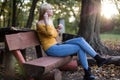 Young blonde woman sitting on a wooden bench in the park, listening to music Royalty Free Stock Photo