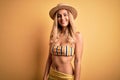 Young beautiful blonde woman on vacation wearing bikini and hat over yellow background with a happy and cool smile on face Royalty Free Stock Photo