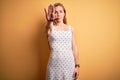 Young beautiful blonde woman on vacation wearing summer dress over yellow background doing stop sing with palm of the hand Royalty Free Stock Photo