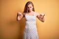 Young beautiful blonde woman on vacation wearing summer dress over yellow background Pointing down looking sad and upset, Royalty Free Stock Photo