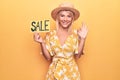 Young beautiful blonde woman on vacation wearing summer hat holding sale banner doing ok sign with fingers, smiling friendly Royalty Free Stock Photo