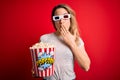 Young beautiful blonde woman watching movie using 3d glasses eating popcorn snack cover mouth with hand shocked with shame for