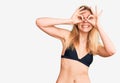 Young beautiful blonde woman wearing bikini doing ok gesture like binoculars sticking tongue out, eyes looking through fingers Royalty Free Stock Photo