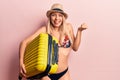 Young beautiful blonde woman wearing bikini and hat holding cabin bag screaming proud, celebrating victory and success very Royalty Free Stock Photo