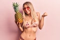 Young beautiful blonde woman wearing bikini and sunglasses holding pineapple screaming proud, celebrating victory and success very Royalty Free Stock Photo