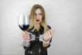 Young beautiful blonde woman wearing black leather jacket drinks wine and shows handcuffed arms on isolated white Royalty Free Stock Photo