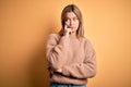 Young beautiful blonde woman wearing brown sweater over yellow isolated background with hand on chin thinking about question, Royalty Free Stock Photo