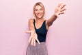 Young beautiful blonde woman wearing casual black t-shirt standing over pink background looking at the camera smiling with open Royalty Free Stock Photo