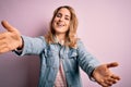 Young beautiful blonde woman wearing casual denim jacket standing over pink background looking at the camera smiling with open Royalty Free Stock Photo